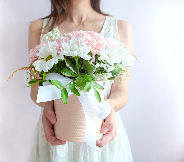 La giovane donna dà un mazzo di fiori in un cestino. Sposa con un mazzo di fiori in un abito da sposa bianco su sfondo chiaro.