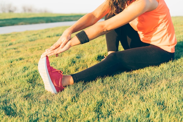 La giovane donna del corridore che allunga le gambe prima dell'esecuzione in un parco. Chiuda sulla ragazza atletica e in buona salute che indossa le scarpe da tennis bianche e rosa.