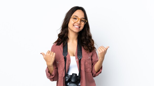 La giovane donna del fotografo sopra la parete bianca con i pollici aumenta il gesto e sorridere