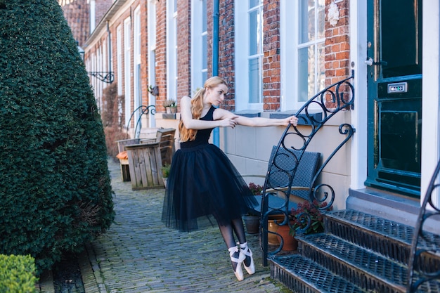 La giovane donna della ballerina con capelli rossi in costume di balletto e scarpe da punta è in bella posa ballare sulla strada.