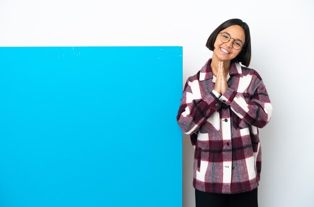 La giovane donna della corsa mista con un grande cartello blu isolato su fondo bianco tiene insieme il palmo. La persona chiede qualcosa