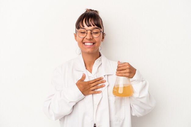 La giovane donna dello scienziato della corsa mista che tiene una provetta isolata su fondo bianco ride ad alta voce tenendo la mano sul petto.