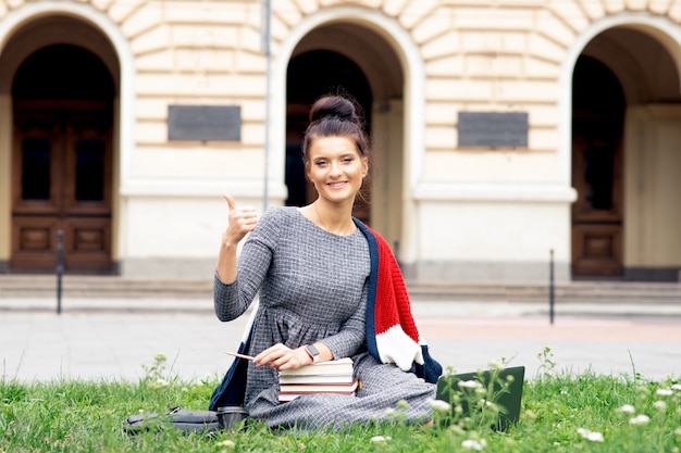 La giovane donna dello studente sta mostrando il pollice su vicino all'università.