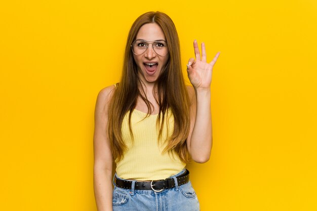 La giovane donna dello zenzero di redhead con freckless sbatte le palpebre un occhio e tiene un gesto giusto con la mano.