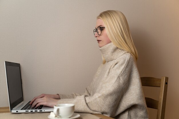 La giovane donna di affari attraente della donna lavora dietro un computer portatile con una tazza di caffè