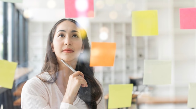 La giovane donna di affari attraente di smiley che utilizza le note appiccicose in parete di vetro per scrivere il piano aziendale di strategia allo sviluppo cresce a successx9