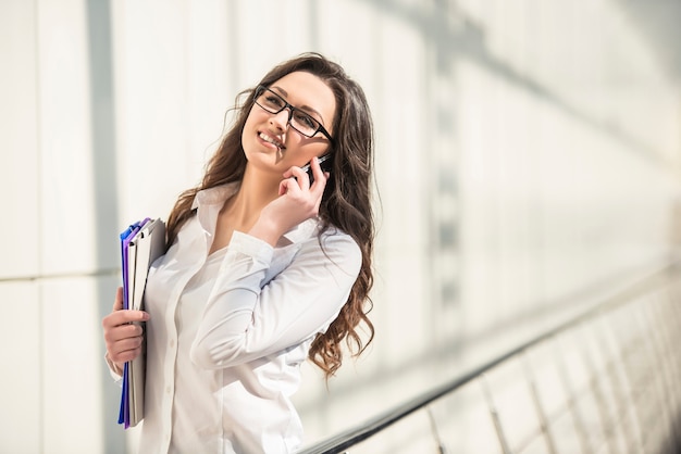 La giovane donna di affari che parla sul telefono e tiene la cartella.