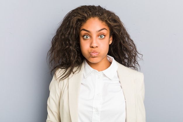 La giovane donna di affari dell'afroamericano soffia le guance, ha espressione stanca. Concetto di espressione facciale.