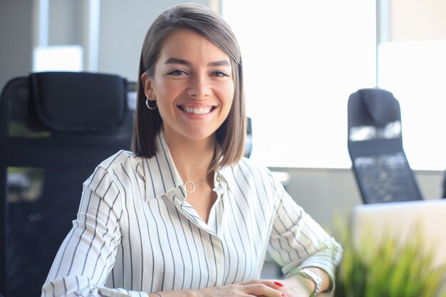 La giovane donna di affari graziosa lavora sul computer portatile nell'ufficio moderno luminoso.