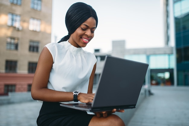 La giovane donna di affari utilizza il computer portatile contro l'edificio per uffici.