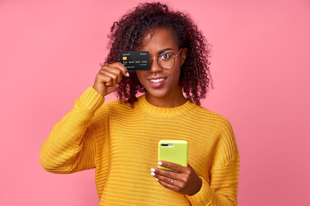 La giovane donna di colore mantiene la carta di credito in plastica utilizza lo smartphone con l'applicazione di mobile banking