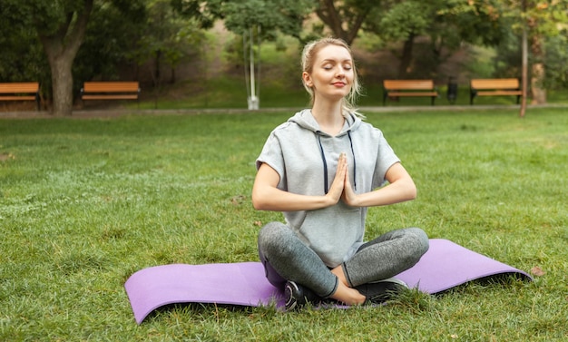 La giovane donna di forma fisica medita mentre si siede sulla stuoia di tna nel parco. Posa di yoga di pratica della donna magra. Uno stile di vita sano