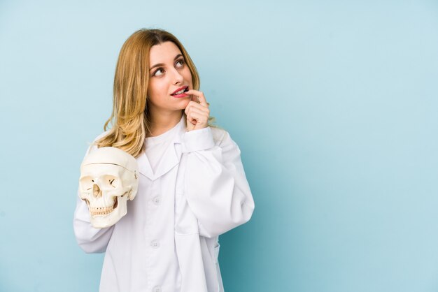 La giovane donna di medico che tiene un cranio ha isolato il pensiero rilassato a qualcosa che esamina uno spazio della copia.