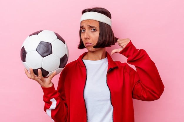 La giovane donna di razza mista che gioca a calcio isolata sul muro rosa si sente orgogliosa e sicura di sé, esempio da seguire.
