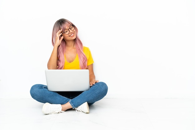 La giovane donna di razza mista con un computer portatile con i capelli rosa seduta sul pavimento isolato su sfondo bianco ha realizzato qualcosa e intendendo la soluzione