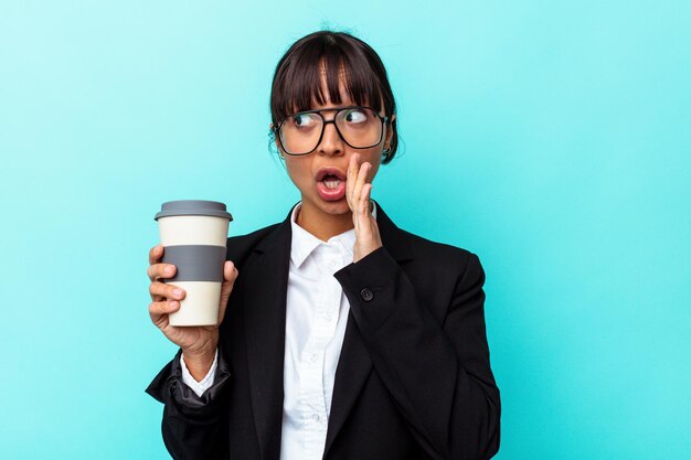 La giovane donna di razza mista d'affari che tiene un caffè isolato su sfondo blu sta dicendo una notizia segreta di frenata calda e sta guardando da parte