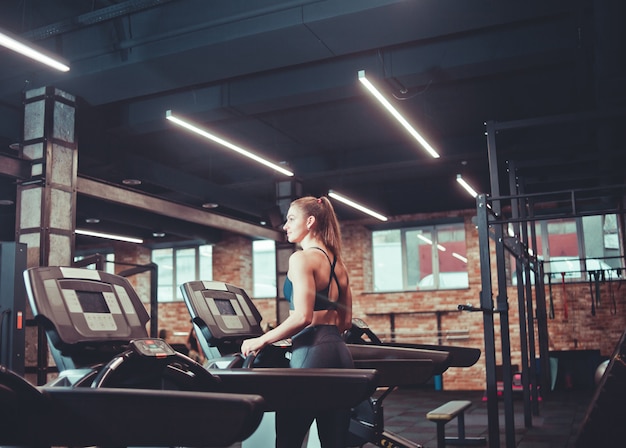 La giovane donna di sport che fa l'allenamento cardio sulla pedana mobile. In esecuzione sul tapis roulant in palestra.