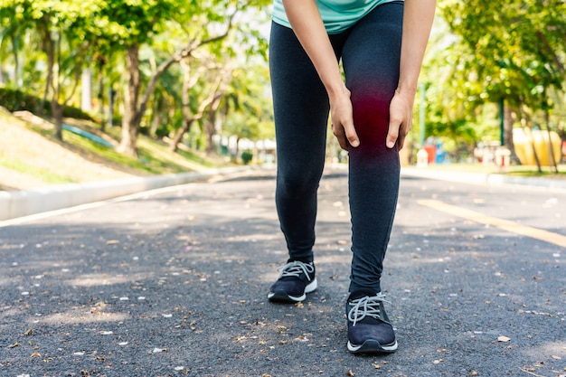 La giovane donna di sport tiene il suo ginocchio danneggiato dentro all&#39;aperto.