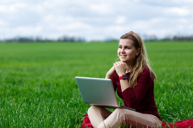 La giovane donna di successo è seduta sull'erba verde con un computer portatile in mano. Lavora sulla natura. Studentessa che lavora in un luogo appartato. Nuove idee imprenditoriali