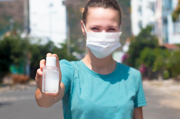 La giovane donna disinfetta le mani, ragazza nella mascherina medica protettiva sulla bottiglia di esposizione del fronte con disinfettante