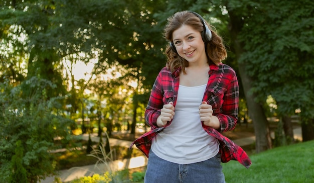 La giovane donna divertente allegra ascolta la musica con le cuffie nel parco all'alba.