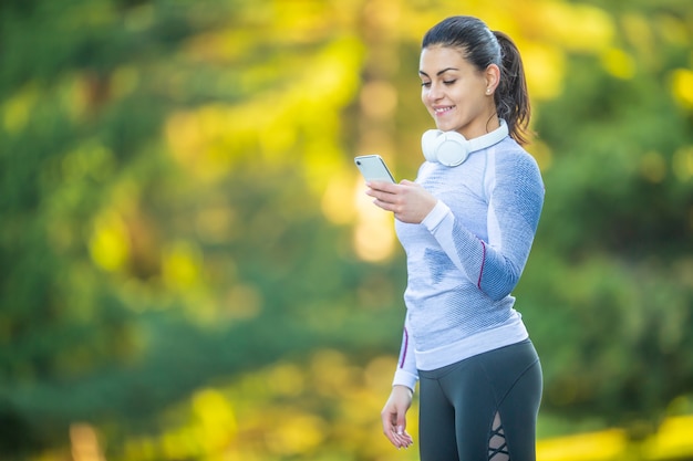 La giovane donna dopo l'addestramento controlla l'inseguitore di sport. Cuffie e smartphone di biancheria intima termica per il concetto di fitness.