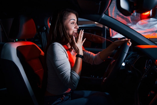 La giovane donna è all'interno di un'automobile moderna nuova di zecca con illuminazione rossa.