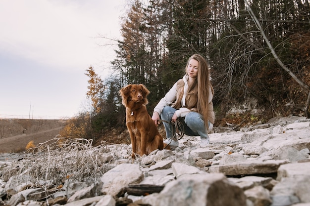 La giovane donna e il cane da riporto camminano sulla riva del fiume alla stagione autunnale