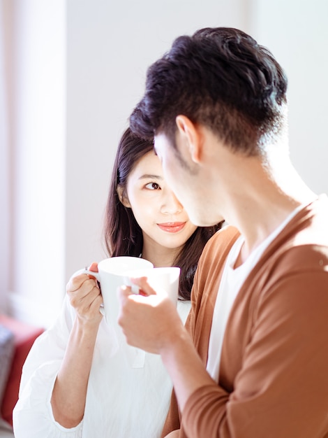 La giovane donna e l'uomo asiatici si divertono a trascorrere del tempo insieme a casa con una tazza di caffè in mano.