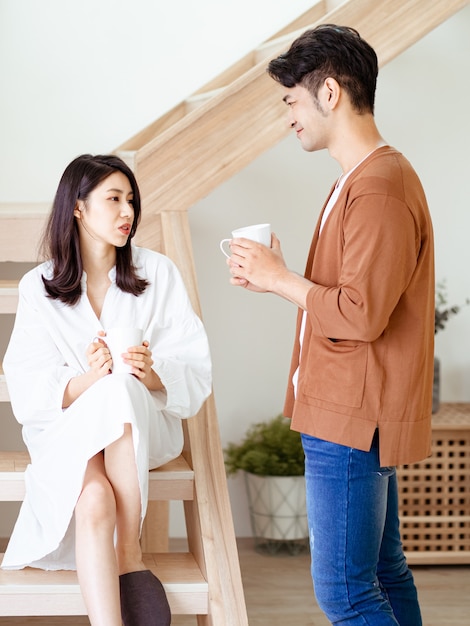 La giovane donna e l'uomo asiatici si divertono a trascorrere del tempo insieme a casa con una tazza di caffè in mano.