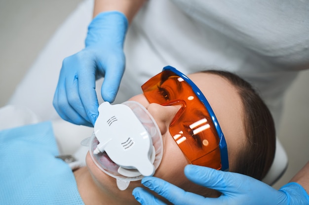 La giovane donna è sdraiata sulla poltrona del dentista con uno strumento speciale in bocca e indossa occhiali protettivi sotto la supervisione del dentista