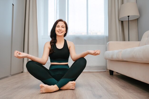 La giovane donna è seduta sul pavimento in una stanza facendo yoga stretchingconcept stile di vita sano