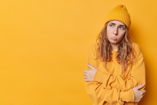 La giovane donna europea frustrata guarda tristemente lontano si sente offesa indossa un maglione casual e il cappello si sente dispiaciuta indossa un maglione casual e un cappello isolato su sfondo giallo spazio vuoto per il tuo promo