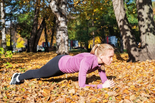 La giovane donna fa esercizi di plancia nel parco Sport fuori in autunno