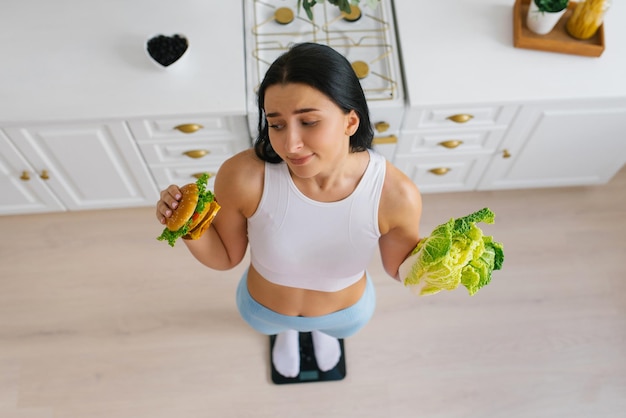 La giovane donna fa una scelta tra cibo sano e malsano e si trova sulla bilancia