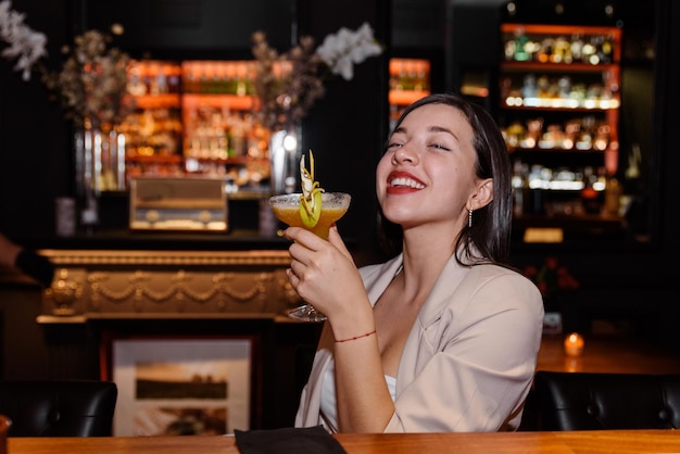 La giovane donna felice beve un cocktail seduta al bancone di un bar