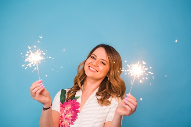 La giovane donna felice con le stelle filanti celebra e ride sulla parete blu