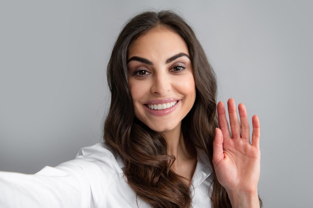 La giovane donna felice eccitata isolata sopra fondo grigio fa il selfie dalla macchina fotografica