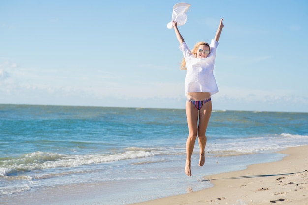 La giovane donna felice salta sulla spiaggia