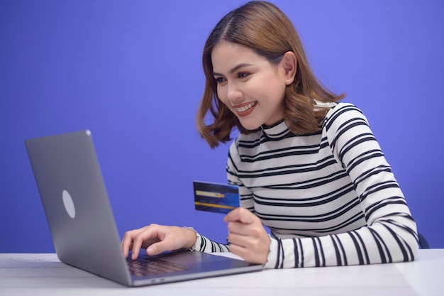 La giovane donna felice sta acquistando online tramite computer portatile, con in mano una carta di credito