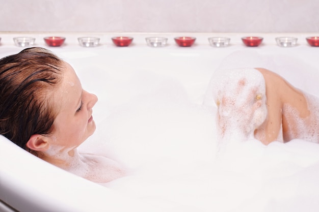 La giovane donna gode della schiuma da bagno nella vasca da bagno.