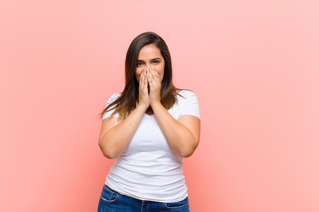 La giovane donna graziosa che sembra felice, allegra, fortunata e sorpresa copre la bocca con entrambe le mani sopra la parete rosa