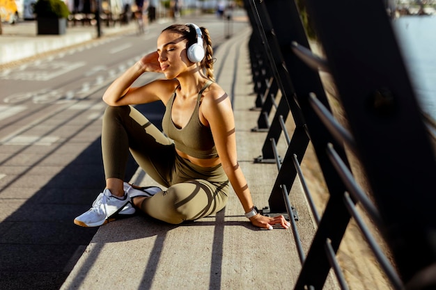 La giovane donna graziosa con gli auricolari si prende una pausa dopo aver corso nell'area urbana
