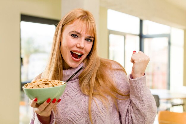 La giovane donna graziosa con una ciotola dei fiocchi della prima colazione all'interno domestico