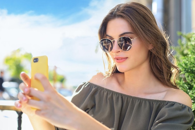 La giovane donna graziosa del brunette all'aperto nella città di estate prende un selfie dal telefono cellulare