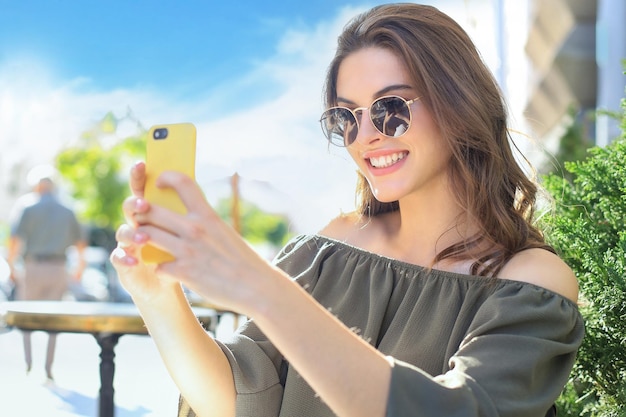 La giovane donna graziosa del brunette all'aperto nella città di estate prende un selfie dal telefono cellulare