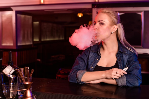 La giovane donna graziosa fuma una sigaretta elettronica al bar di vape. Negozio di vaporizzatori.