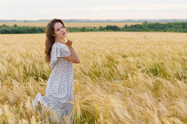 La giovane donna graziosa in vestito posa sul campo di grano