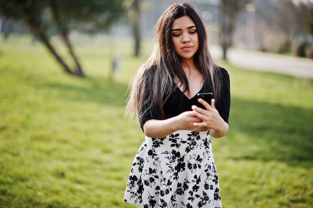 La giovane donna graziosa porta sulle cime e sulla gonna poste alla via con il telefono cellulare.