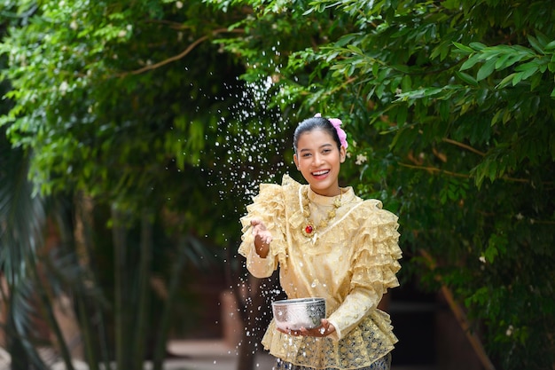 La giovane donna graziosa si veste con bei costumi tailandesi che spruzzano acqua nei templi e preserva la buona cultura del popolo tailandese durante il festival di Songkran Giorno della famiglia di Capodanno tailandese ad aprile